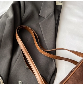 Macro shot of brown suede bowling bag with twin leather straps on a grey blazer