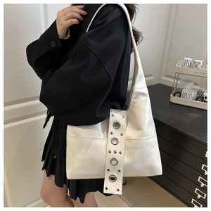 Detail of white glossy shoulder bag featuring wide strap with metal eyelet decorations