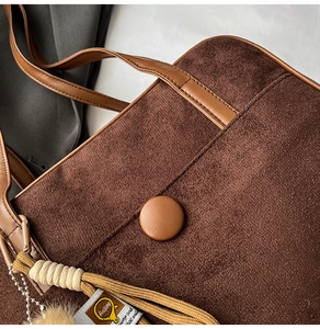 Close-up of brown suede tote bag featuring smooth leather handles and plush charm detail