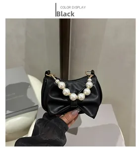 Detail of mini black bow handbag with decorative pearl handle and gold hardware