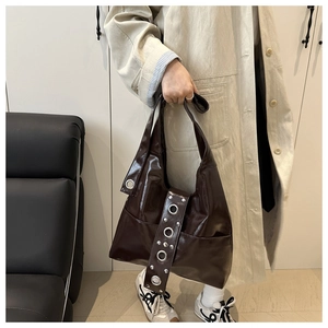 Detail of dark brown patent leather hobo bag featuring silver grommets and oversized rivets