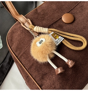 Close-up of brown matte tote bag with cute plush monster charm and leather tag