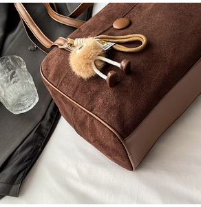 Close-up of brown suede tote bag featuring leather stitching and a cute doll pendant