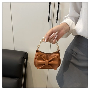 Detail of brown mini handbag featuring large bow design and white pearl beaded handle