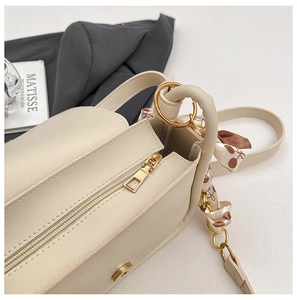 Close-up of cream crossbody bag featuring golden hardware and floral silk scarf detail