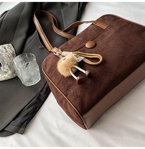 Detailed macro shot of dark brown suede tote bag with leather straps and plush charm