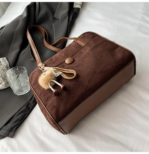 Detail of a brown suede hobo bag with leather trim and a decorative plush charm