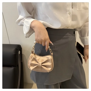 Close-up of beige mini bow handbag with elegant pearl handle and faux leather texture