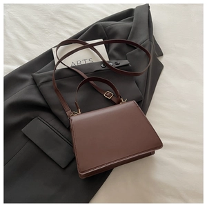 Détail du sac à main en cuir marron foncé avec boucles dorées sur tissu gris