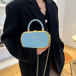 Light blue oval handbag with gold chain strap and twisted handle held by a model