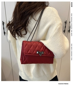 Detailed view of a red quilted shoulder bag with chain strap on a cream knit sweater