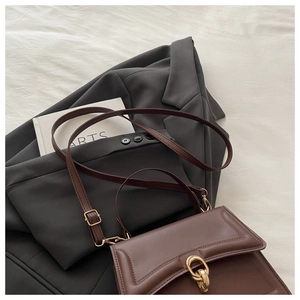 Détail d'un sac à bandoulière en cuir marron foncé avec boucle dorée sur un blazer