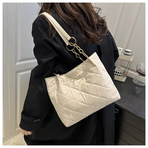 Close-up of beige quilted tote bag featuring metal logo and chain leather strap detail