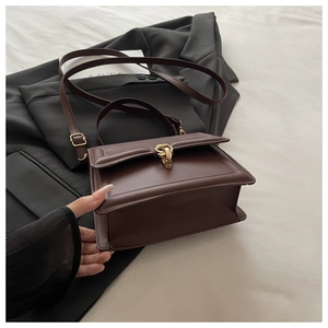 Détail du sac bandoulière marron foncé structuré avec boucle dorée sur un fond de blazer
