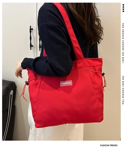 Detail of red large capacity tote bag featuring fashion label and side drawstring design