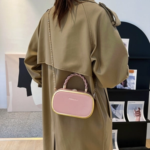 Pink box crossbody bag with woven handle and gold chain strap shown on a model