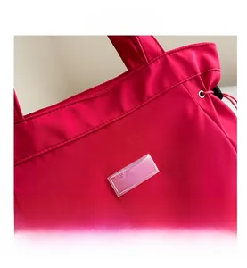 Detail of red water-resistant nylon tote bag featuring a transparent FASHION label and drawstring