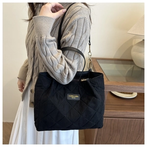 Detail of black quilted tote bag featuring gold brand label and metal chain strap accent