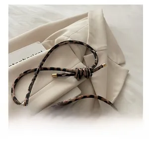 Detail of slim leopard print strap with gold metal ends and knot on beige blazer