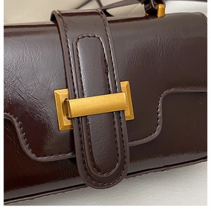 Détail d'un sac à main marron foncé brillant avec boucle en métal doré mat et surpiqûres