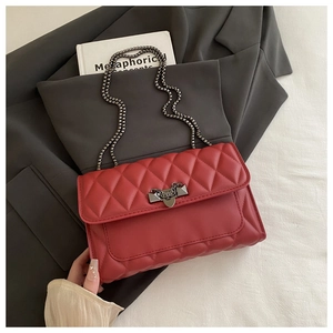 Close-up of red quilted shoulder bag with geometric metal clasp and chain strap
