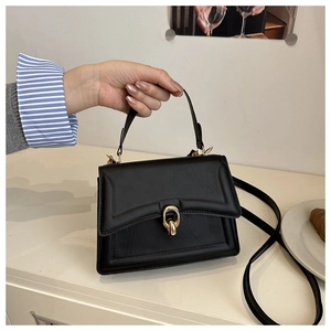 Gros plan d'un sac bandoulière noir avec fermoir anneau doré sur une table blanche