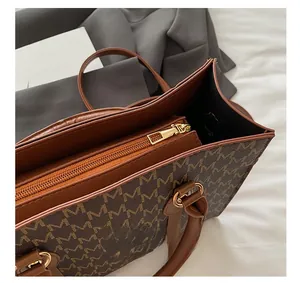 Detail of dark brown tote bag with M-pattern, gold zipper closure and metal hardware