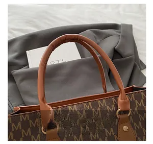 Close-up of brown leather handle and gold hardware on retro M-patterned tote bag