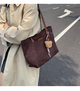 Detail of brown corduroy tote bag with leather straps and plush bear charm