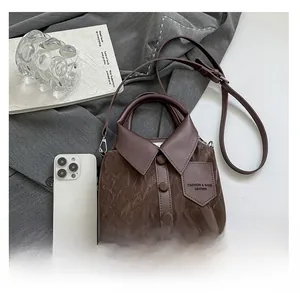 Detailed view of brown shirt-shaped bag showing scale with a smartphone for size reference