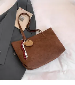 Detail of a brown suede tote bag with a bear charm and elegant decorative rope accessory