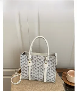 Detail view of white monogram tote bag with gold hardware on brown texture