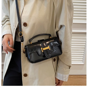 Détail du sac à main noir brillant avec boucle H dorée porté sur trench beige