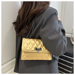 Close-up of quilted light gold crossbody bag with metallic chain and stylish lock