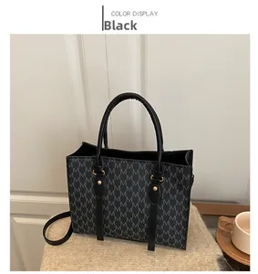 Detail of black tote bag with M-pattern texture and golden cylindrical metal buckle