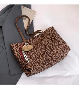 Detailed view of leopard print tote bag with brown straps and plush bear charm