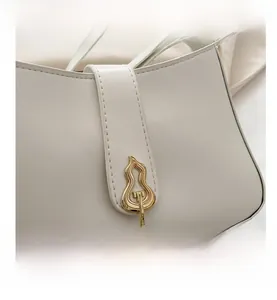 Detail of white leather baguette bag featuring a golden gourd-shaped metal clasp