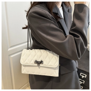 Close-up of a white quilted crossbody bag featuring a unique dark grey metal lock and chain strap