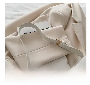 Detail view of cream shoulder bag with golden square buckle and adjustable strap on a blazer
