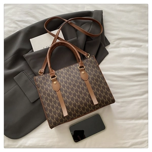 Close-up of brown monogram tote bag with gold hardware on a grey blazer background