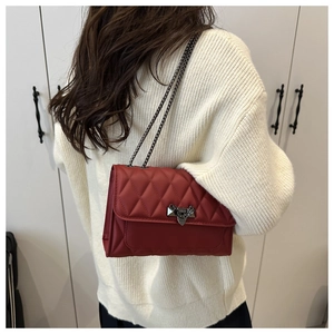Close-up of a red quilted leather crossbody bag with metal chain and buckle on a model