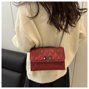 Detail of red quilted shoulder bag with dark metal chain strap and luxury lock clasp