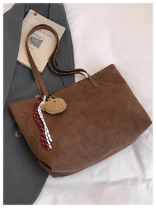 Detail of retro dark brown corduroy tote bag with plush bear charm and leather straps