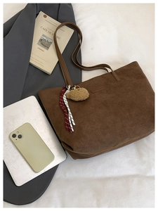 Detailed close-up of brown suede tote bag featuring fuzzy bear charm and tassel detail