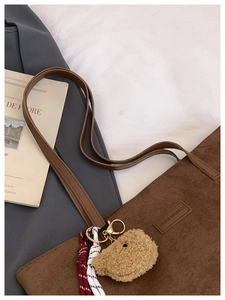 Detail of coffee corduroy tote bag featuring leather straps and a plush bear charm