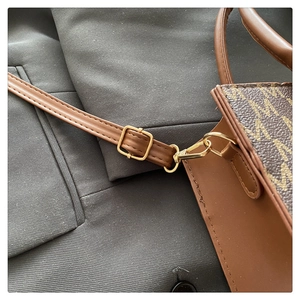 Detail of a brown tote bag featuring embossed M pattern and adjustable gold buckle strap
