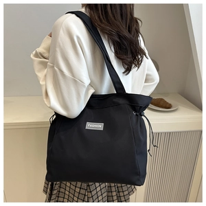 Detailed view of black nylon tote bag with drawstring sides and Fashion label detail