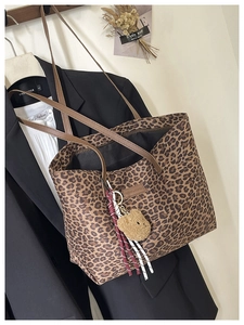 Close-up of leopard print tote bag featuring a leather logo tag and plush bear charm