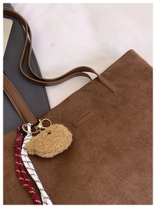 Detail view of brown corduroy tote bag with plush bear charm and fashion label