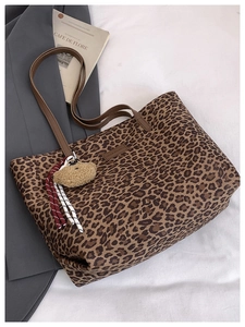 Close-up of leopard print tote bag with leather strap and plush bear charm accessory